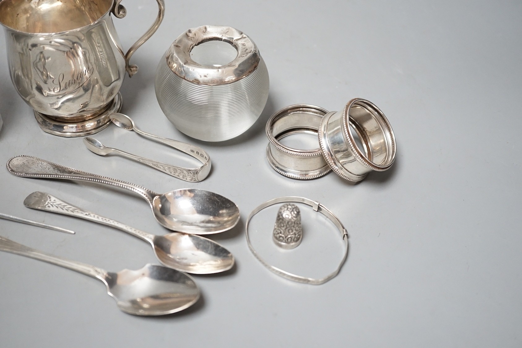 Sundry small silver including a mounted glass match tidy(a.f.), a silver christening mug(a.f.), mounted glass preserve jar, three napkin rings, six items of flatware, thimble T-bar and a sterling bangle.